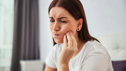 Image of a lady with a painful expression on her face with hands placed on her jaws