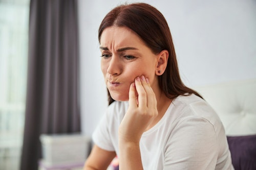 Image of a lady with a painful expression on her face with hands placed on her jaws