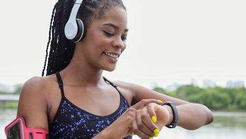 A Black womanwearing headset and using a fitness tracker while running
