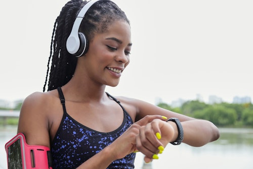 A Black womanwearing headset and using a fitness tracker while running