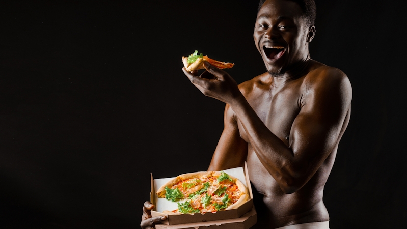Black man with abs and well-toned body  smiling and eating pizza from a pizza box