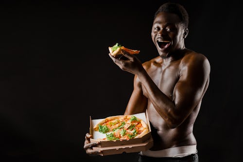 Black man with abs and well-toned body  smiling and eating pizza from a pizza box