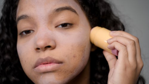 image of a girl with acne applying concealer make up