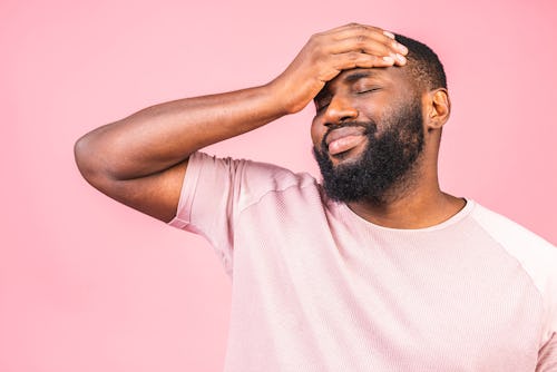 A Black man having headache holdings his hands over his forehead