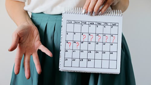 A woman wearing a green colored skirt with a period calendar showing missed period days