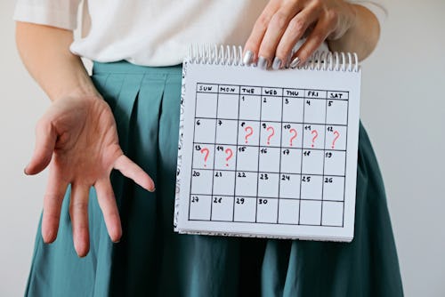 A woman wearing a green colored skirt with a period calendar showing missed period days