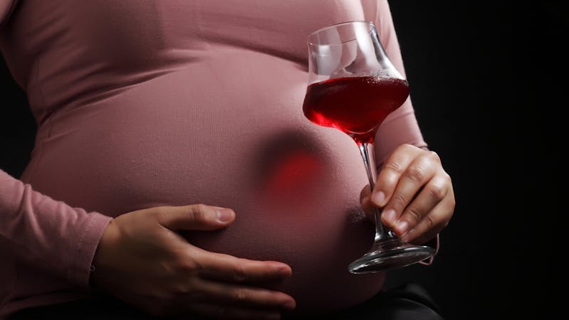 A pregnant woman carrying a glass of zobo drink