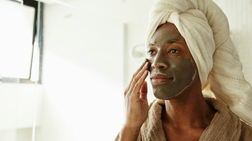 A man standing before a mirror, applying facial mask as part of his skincare routine
