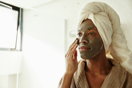 A man standing before a mirror, applying facial mask as part of his skincare routine