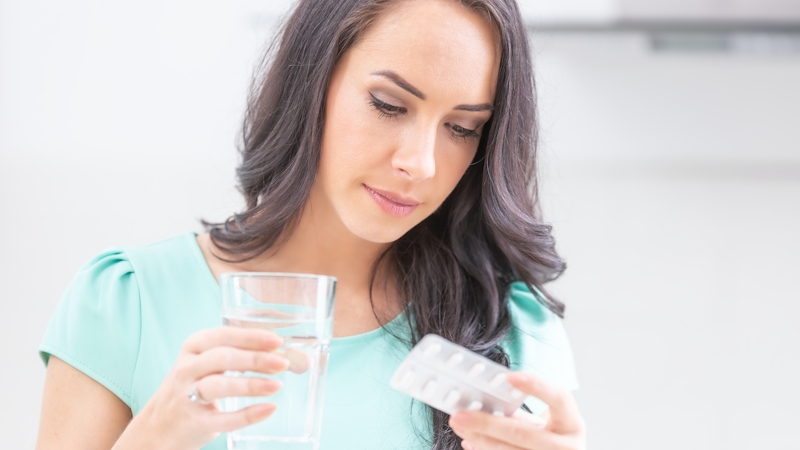 A white woman with long flowing hair holding a glass of water and a medicine tablet