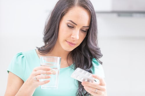 A white woman with long flowing hair holding a glass of water and a medicine tablet