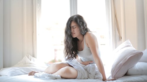 A girl sitting on a bed with white mattress with hands placed on her tummy