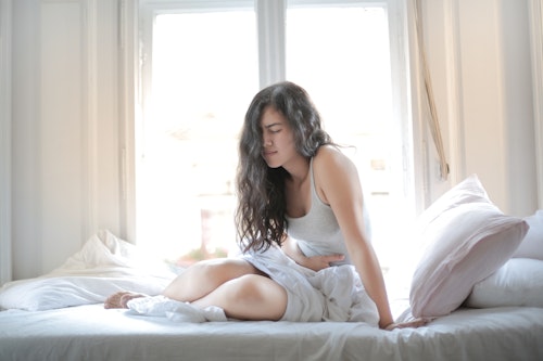 A girl sitting on a bed with white mattress with hands placed on her tummy