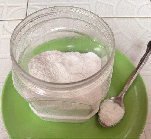 A jar of salt and a spoon with salt placed on a green plate