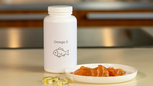 Slices of fish on a plate and a bottle of omega-3 acid supplement placed on a table