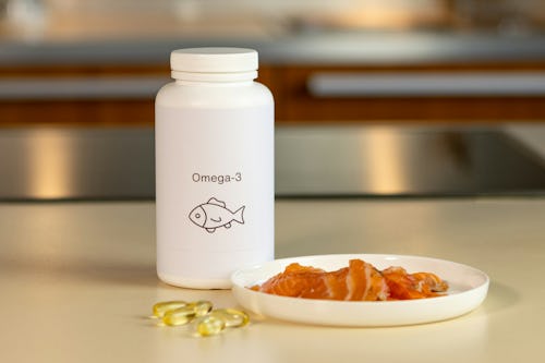 Slices of fish on a plate and a bottle of omega-3 acid supplement placed on a table