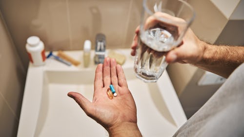 A man holding a glass of water in one hand and two pills in the other hand