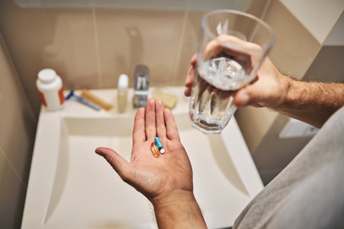 A man holding a glass of water in one hand and two pills in the other hand