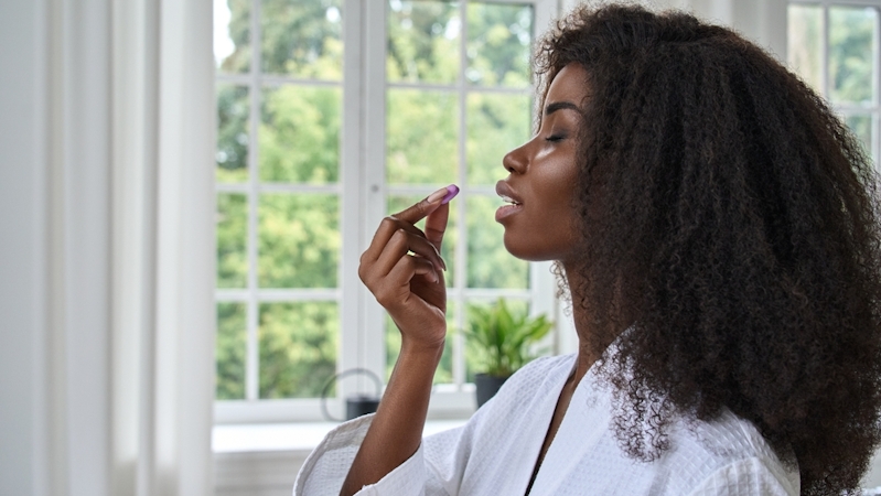 Picture of a Black woman with long hair on a white robe taking a pill