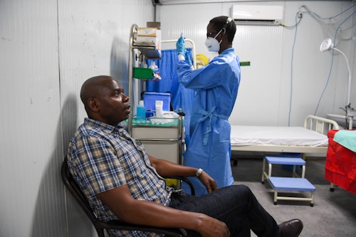 A man sitting on a chair in a hospital room with a doctor wearing a scrub about to give him an injection