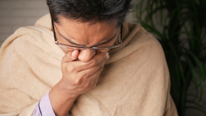 A sick man wearing eye glasses covering his mouth with his hands resisting the urge to vomit