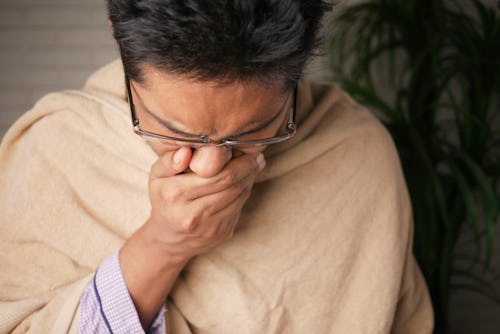 A sick man wearing eye glasses covering his mouth with his hands resisting the urge to vomit