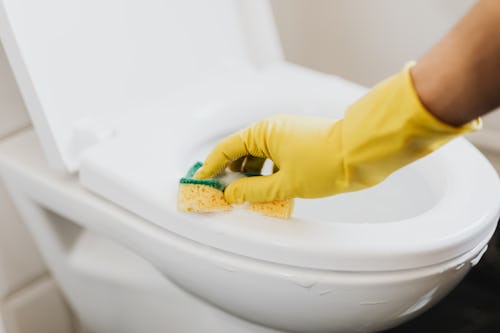 A person wearing hand-gloves washing the toilet