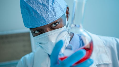 Image of a doctor, wearing a nose mask holding a test tube with a sample for research