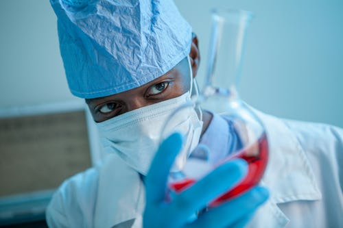 Image of a doctor, wearing a nose mask holding a test tube with a sample for research