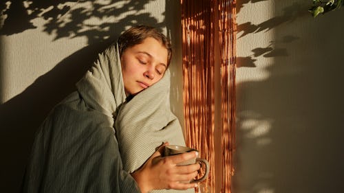 A lady receiving sun outside her porch with a cup of coffee in hands