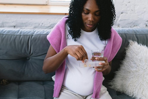 Image of a pregnant woman taking pill holding a glass of water 