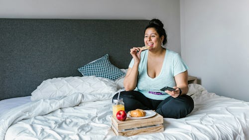 Image of an overweight woman on a bed eating food, and apple drinking from a glass of juice placed on the bed