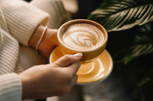 A woman holding a mug cup of creamed coffee