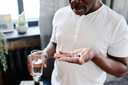 A man holding medication pills and a glass of water