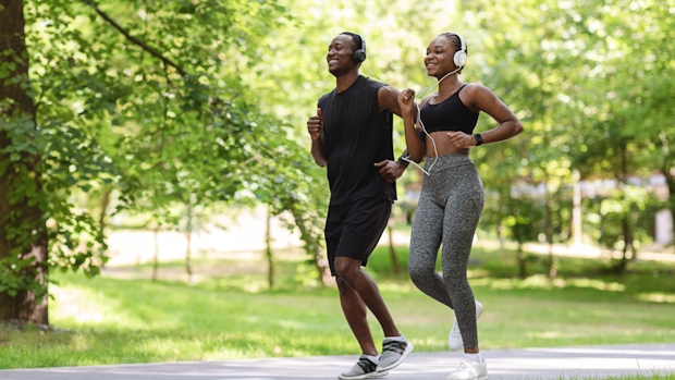 A black man and black woman wearing a headset jogging on a pathway 