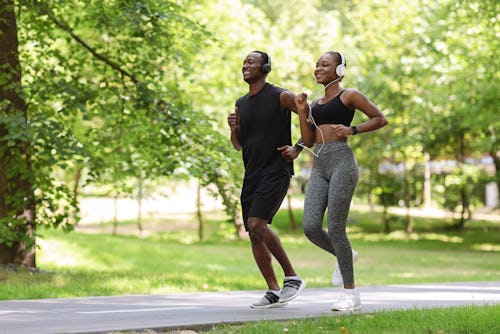 A black man and black woman wearing a headset jogging on a pathway 