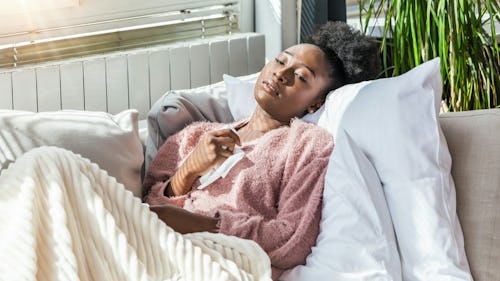 A sick lady lying on a couch wearing knitted sweater with a duvet covering her legs