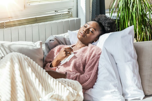 A sick lady lying on a couch wearing knitted sweater with a duvet covering her legs