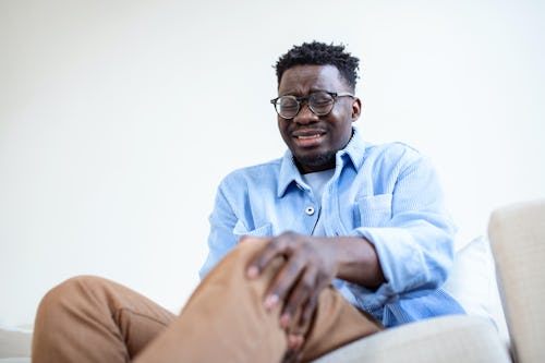 A man wearing an eye glass crying, holding his knees in pain due to chronic inflammation