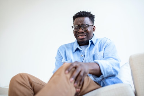 A man wearing an eye glass crying, holding his knees in pain due to chronic inflammation