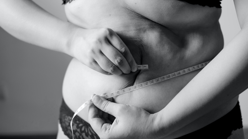 A woman with belly fat measuring her belly with measuring tape