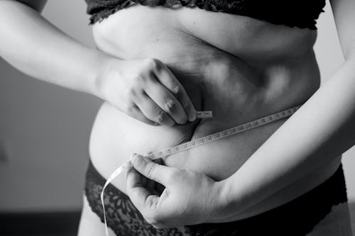 A woman with belly fat measuring her belly with measuring tape