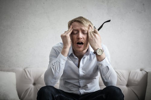 A stressed white man wearing a wrist watch rubbing his forehead with his hands 