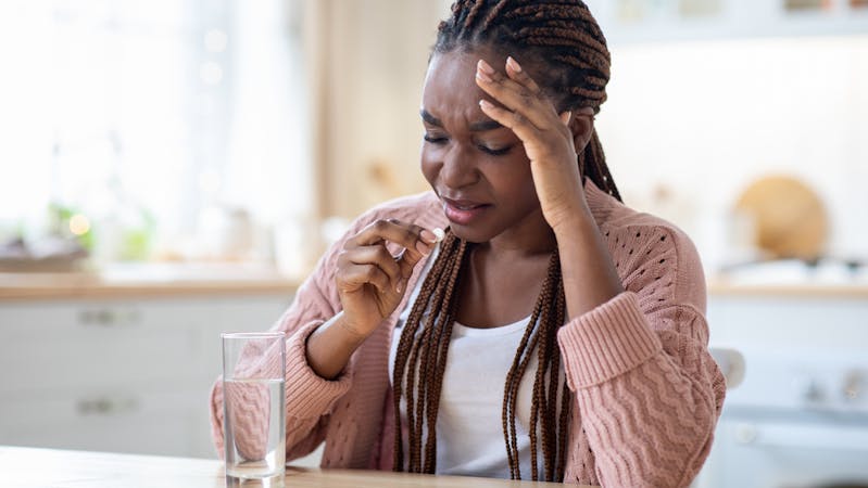 Sad Black girl taking postinor-2 pill with a glass of water