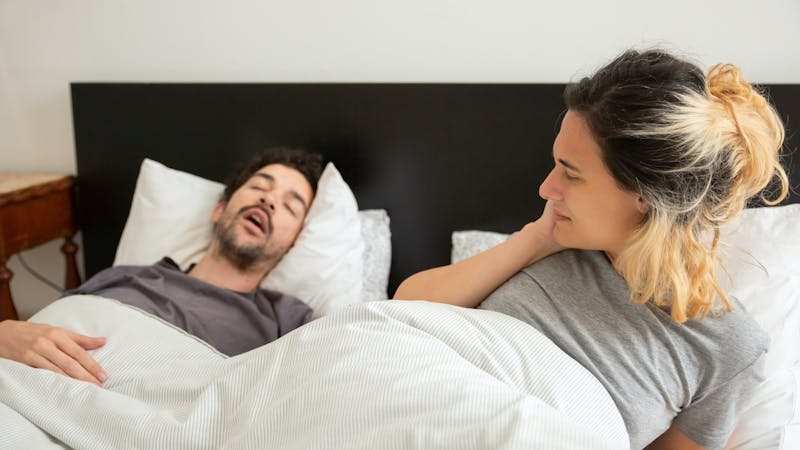 A man snoring while sleeping beside his wife