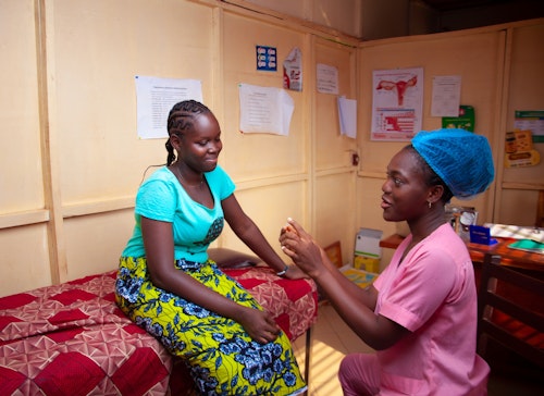 A Black nurse talking to a Black patient who is sitting on a hospital bed