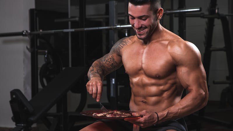 An athletic bodybuilder eating in the gym