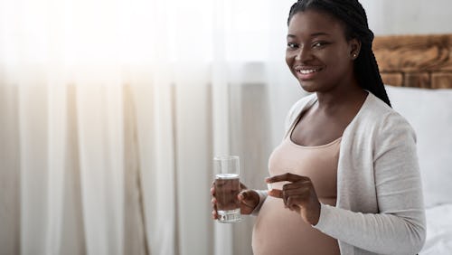 Black pregnant woman taking a pill medication with a glass of water 