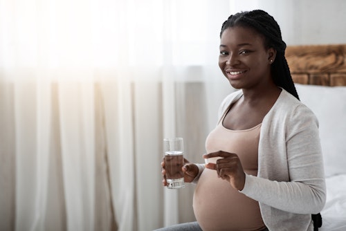 Black pregnant woman taking a pill medication with a glass of water 