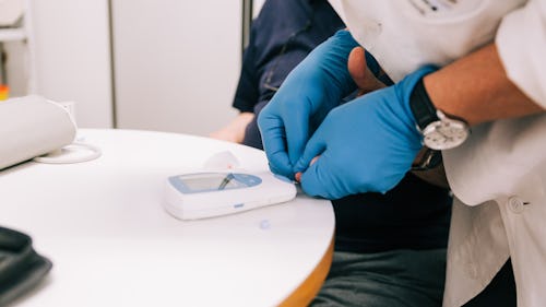 A healthcare professional wearing a handglove using a glucometer to test a patient's blood sample for blood glucose level